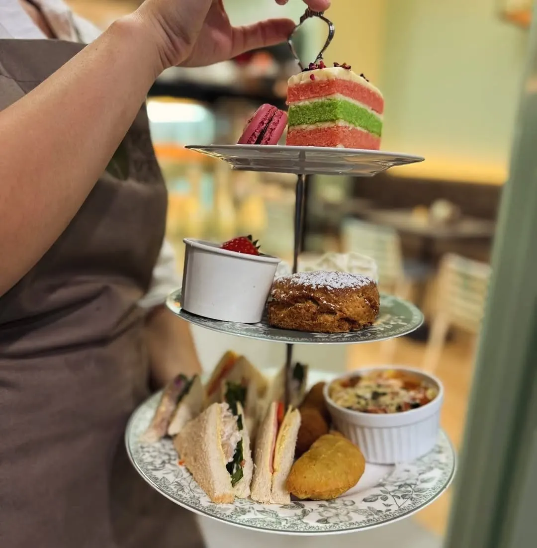 A three-tier stand of ribbon sandwiches, quiche, scones and cake held up by a Köfi Köfi team member