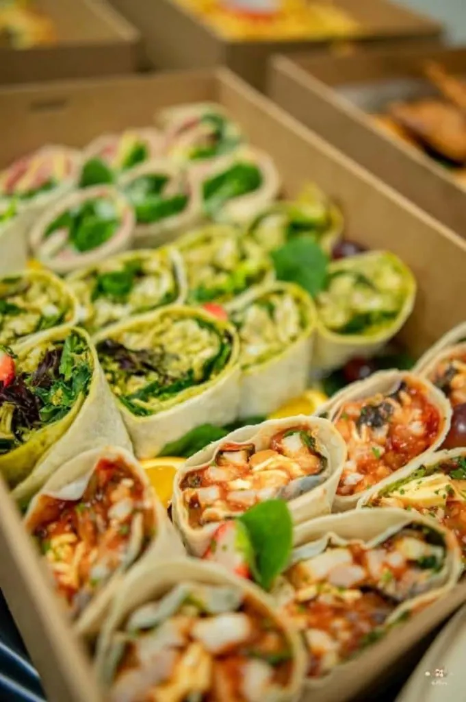 A catering box of fresh wraps, with green vegetable wraps and chicken wraps